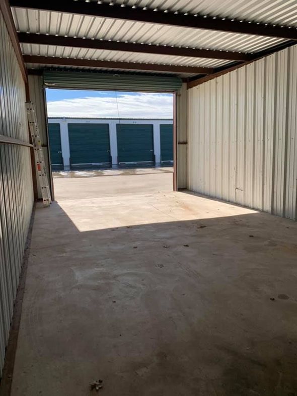Interior view of an empty metal storage unit with the door open, facing a row of other storage units under a blue sky.