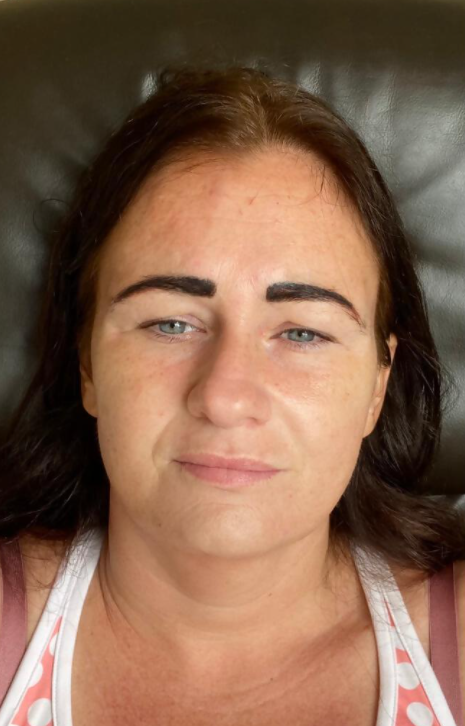 Woman with dark eyebrows and brown hair, looking at the camera. She's wearing a light-colored top.