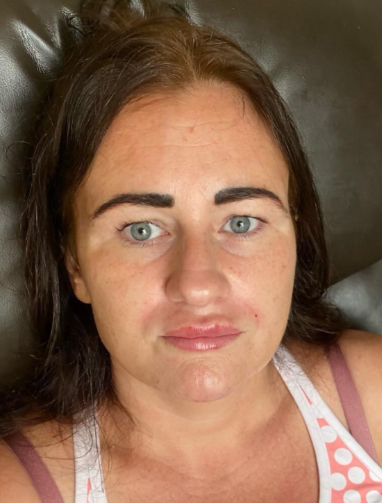 Woman with light blue eyes, dark eyebrows, and brown hair wearing a white and pink top, looking at the camera.