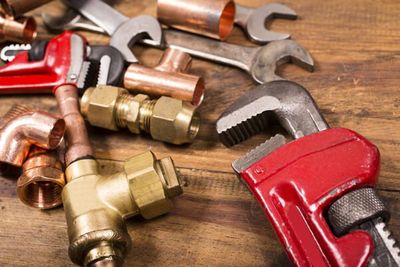 Various construction, DIY, plumber's hand tools and copper and brass plumbing pipes and fittings lie on a rustic wooden table, desk or workbench. Tools include styles of various wrenches. Home improvement, plumbing, construction themes. Great background. Close up.