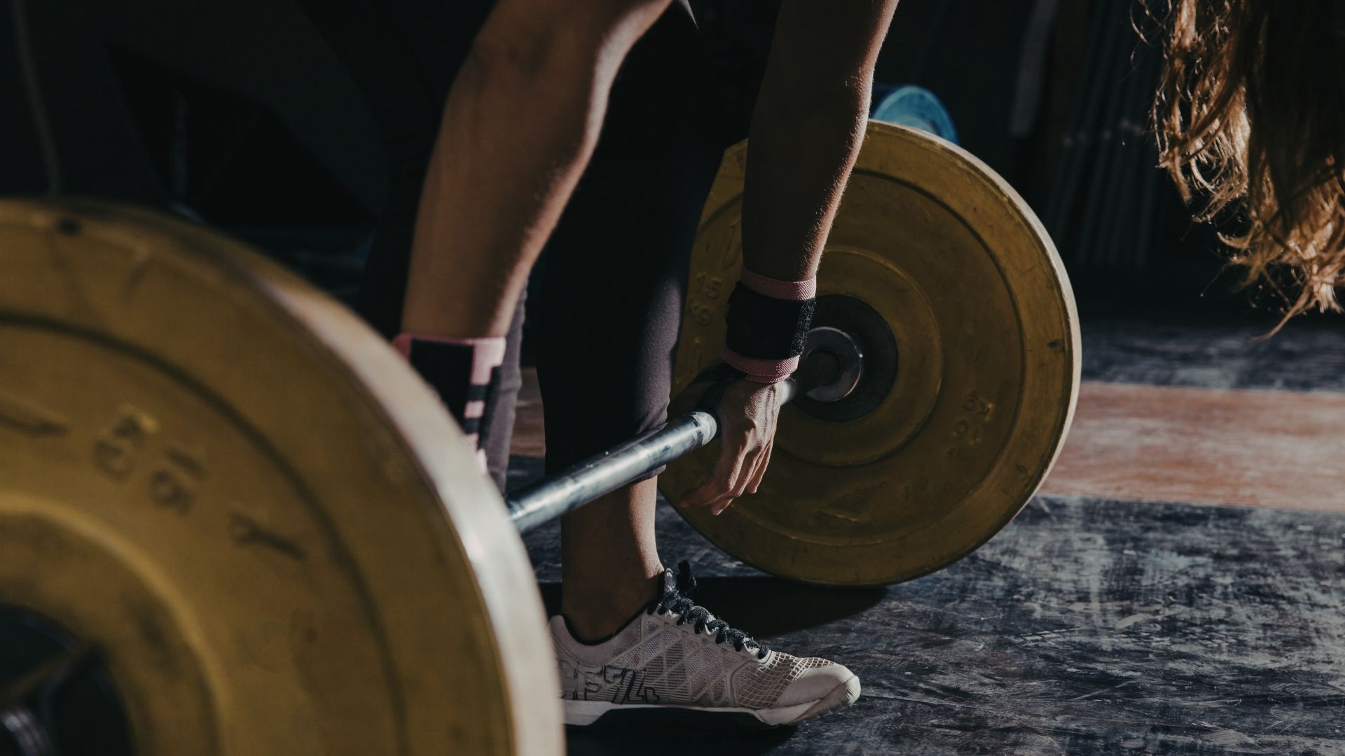 A person prepares to lift a barbell with large yellow plates in a dark gym.