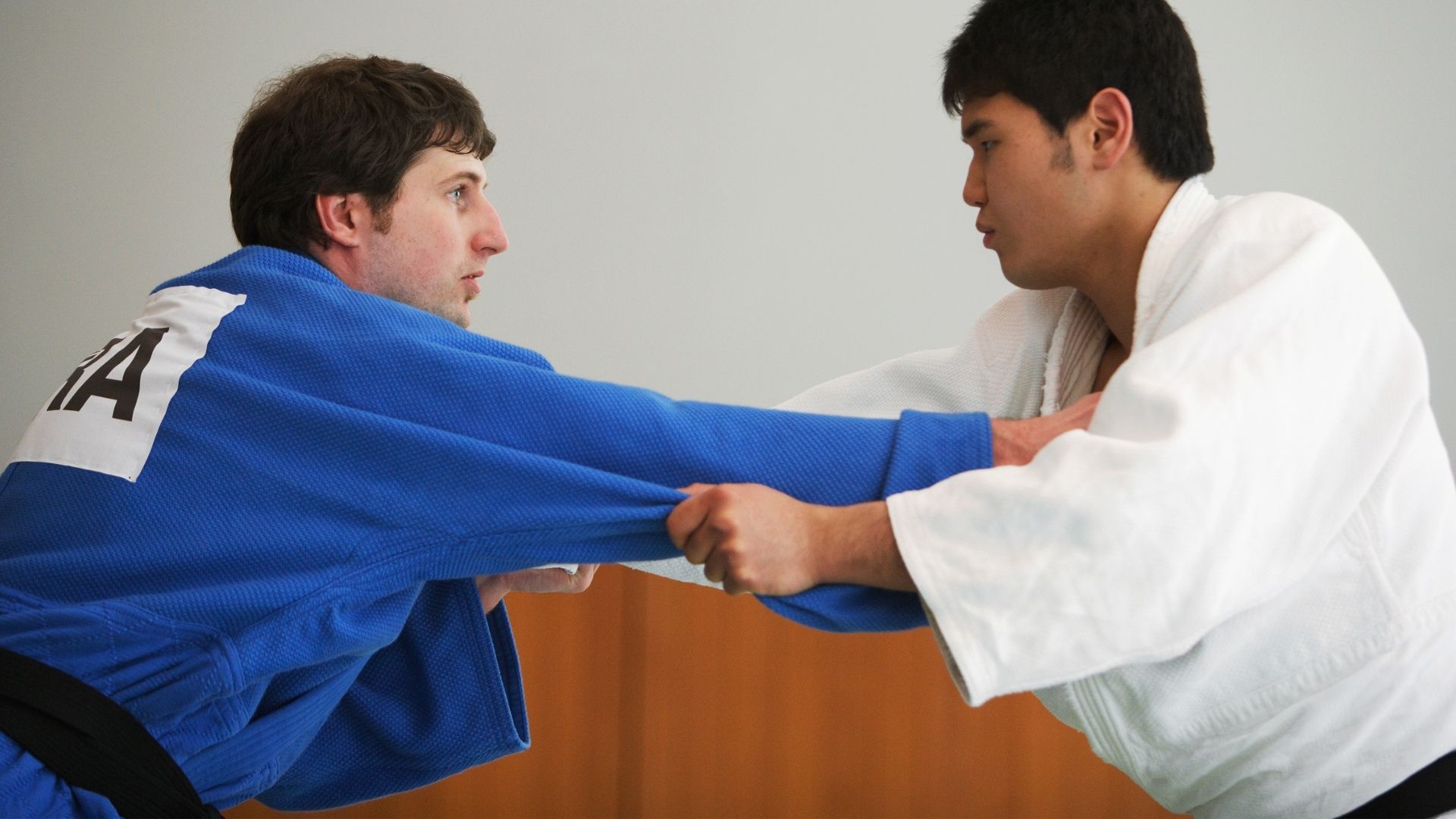 Two judo practitioners in blue and white gis face each other while gripping the opponent's lapel and sleeve.