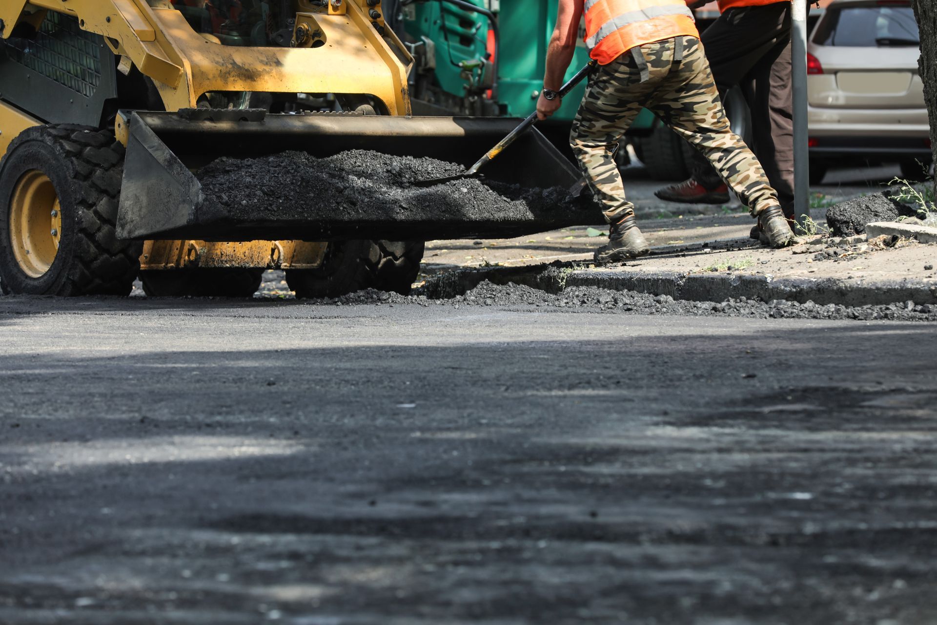 Road construction: Workers shoveling asphalt from a skid steer into a street.