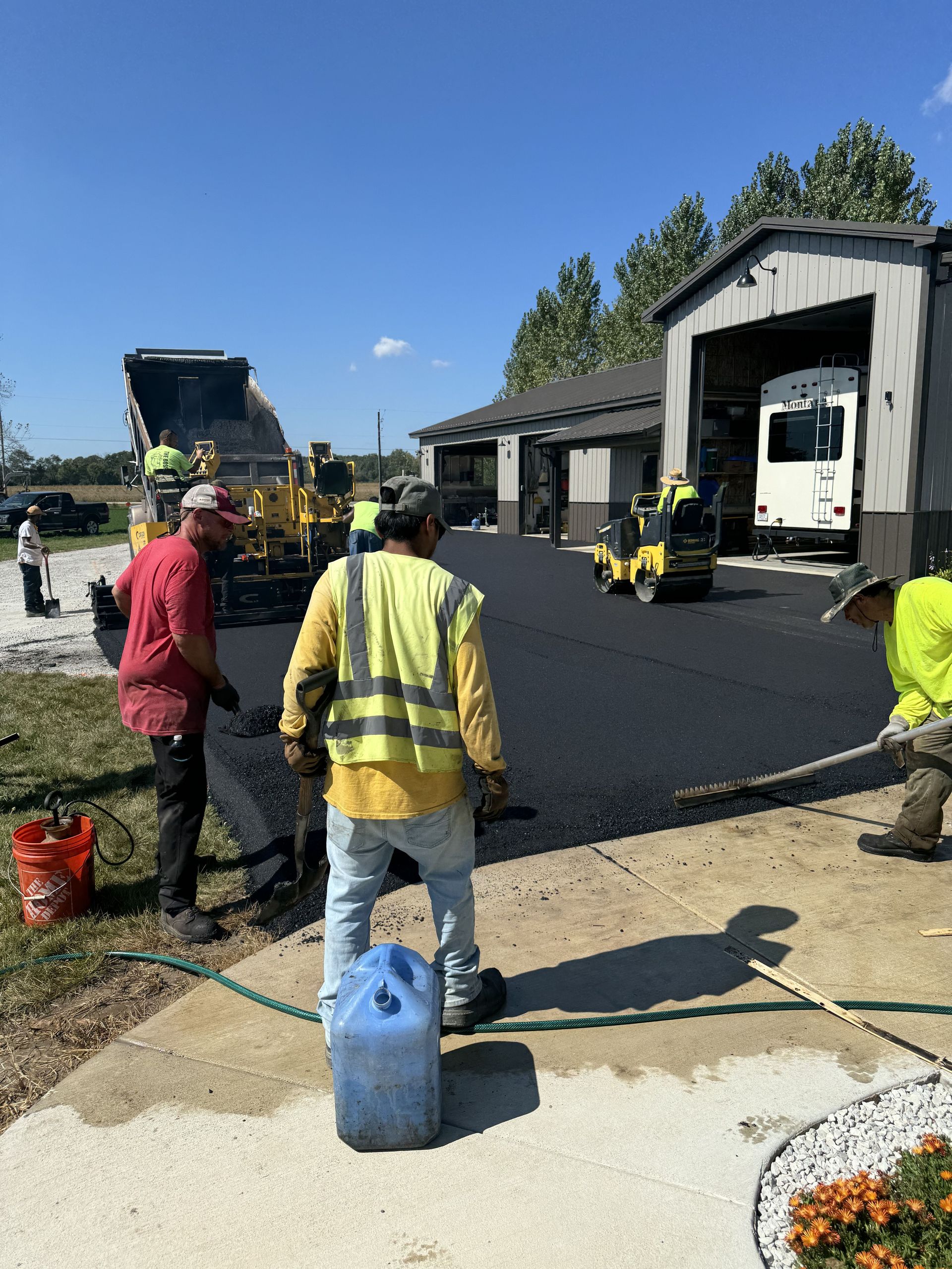 Asphalt paving crew laying blacktop in front of a building on a sunny day.