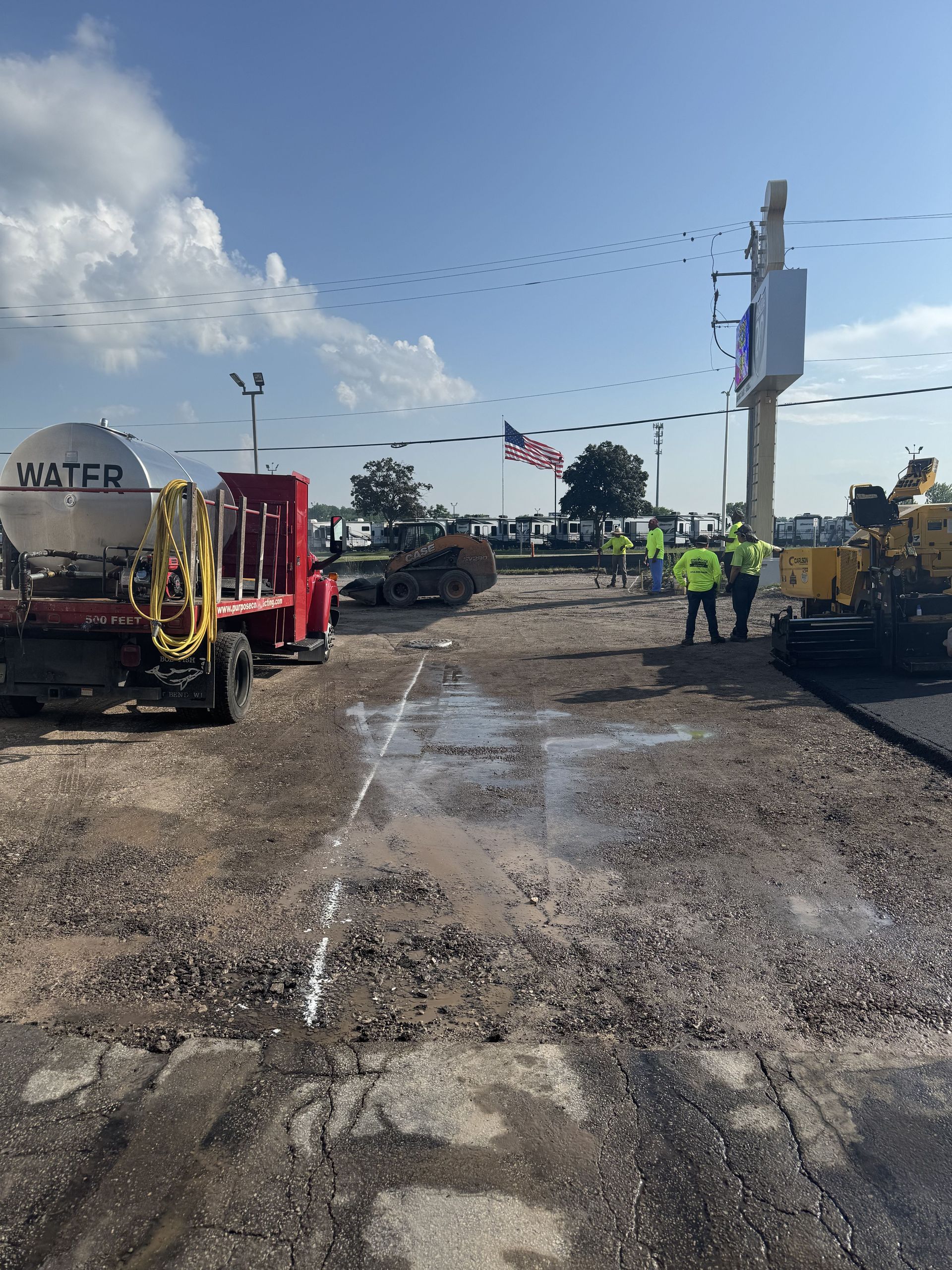 Road construction site with workers in vests, water truck, and equipment.