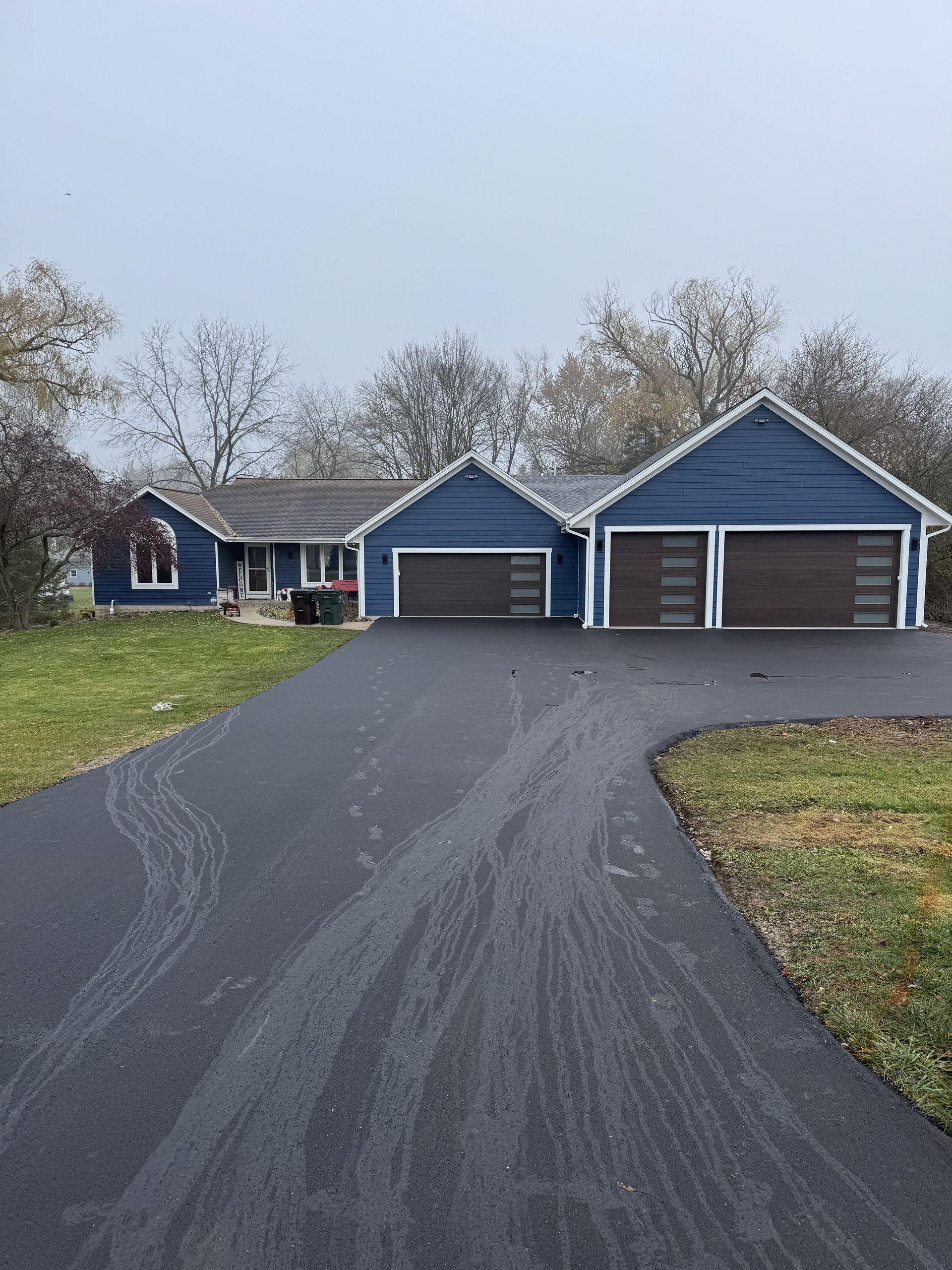 Blue house with two-car garage; long black driveway; overcast day.