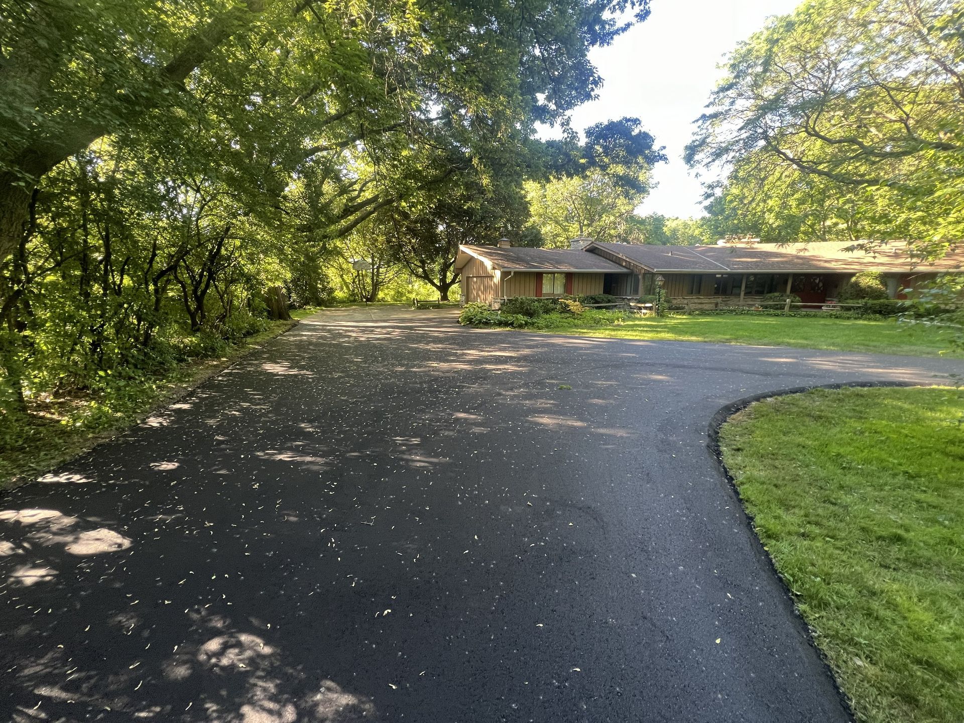 Blue house with two-car garage; long black driveway; overcast day. Show casing high quality residential asphalt paving.