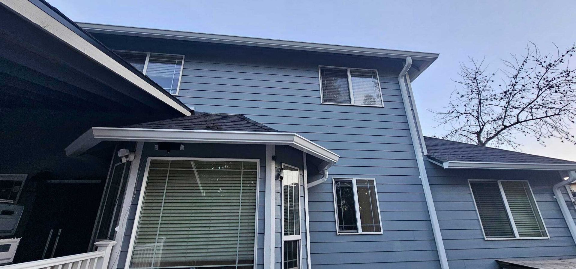 Grey shingled roof with a skylight, trees and a blue sky in the background.
