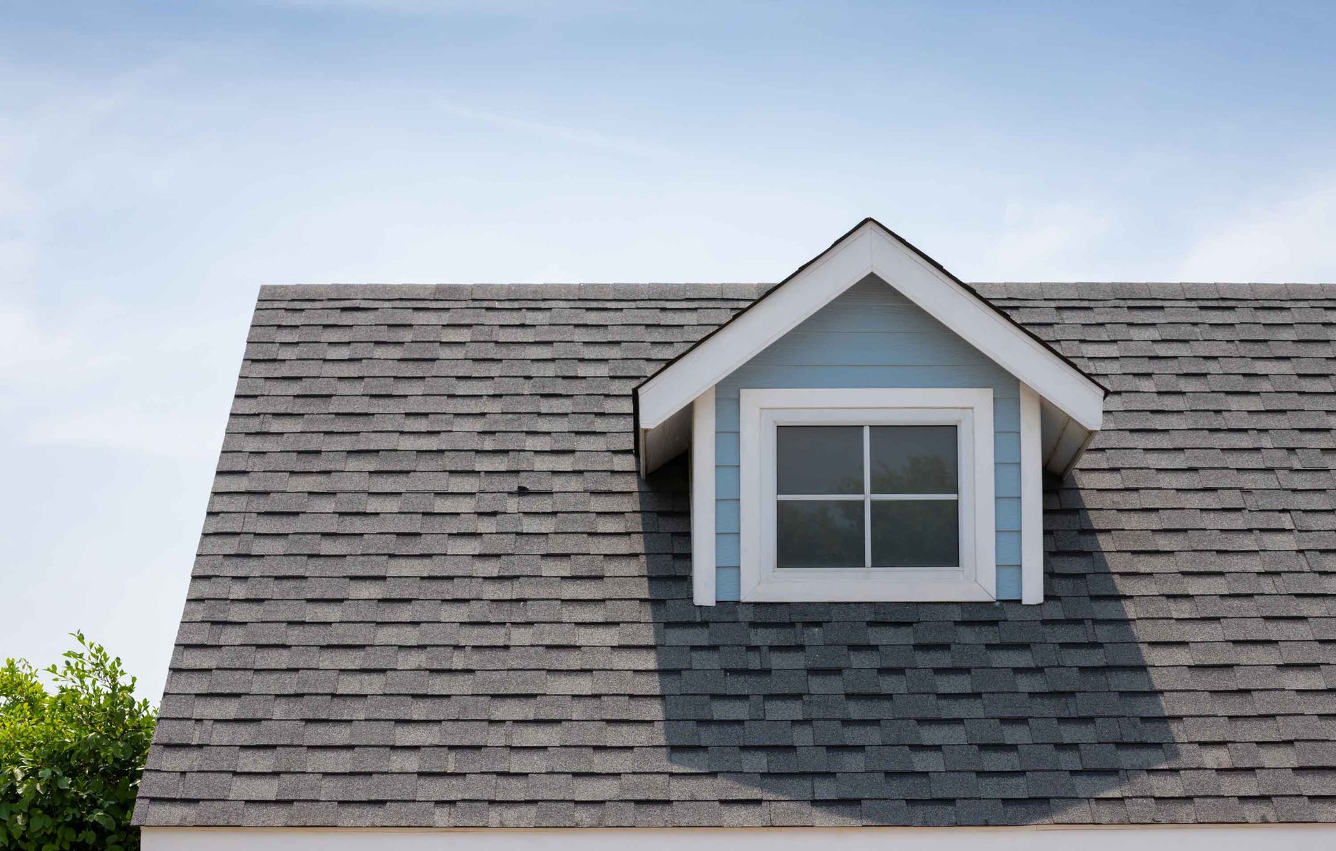 Blue dormer window on a gray shingle roof under a blue sky. Blue dormer window on a gray shingle roof under a blue sky.