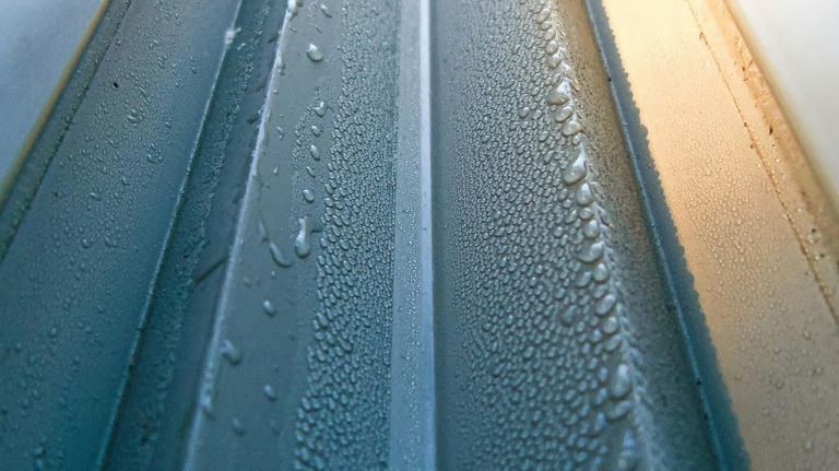 Close-up of a ridged, light gray surface with numerous water droplets clinging to the ridges.
