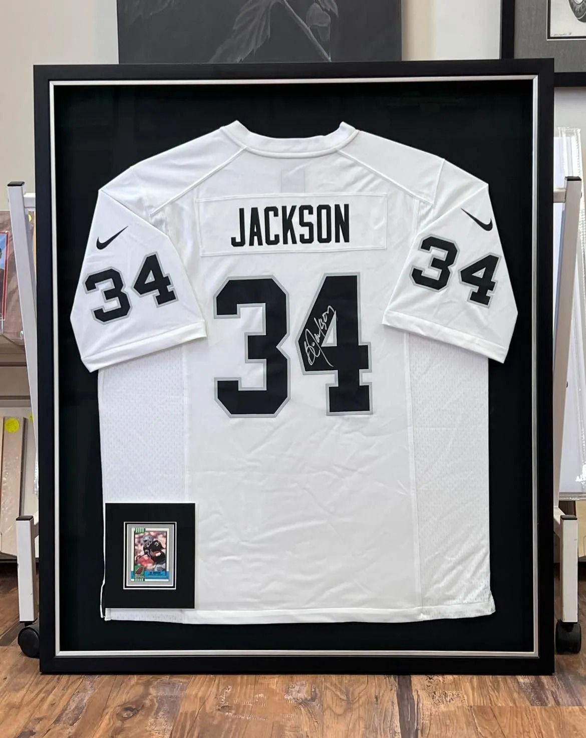 Framed white Jackson #34 football jersey with black lettering and patch, displayed on a wall.