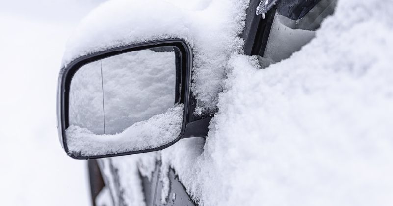 the side mirror of a car is covered in snow .
