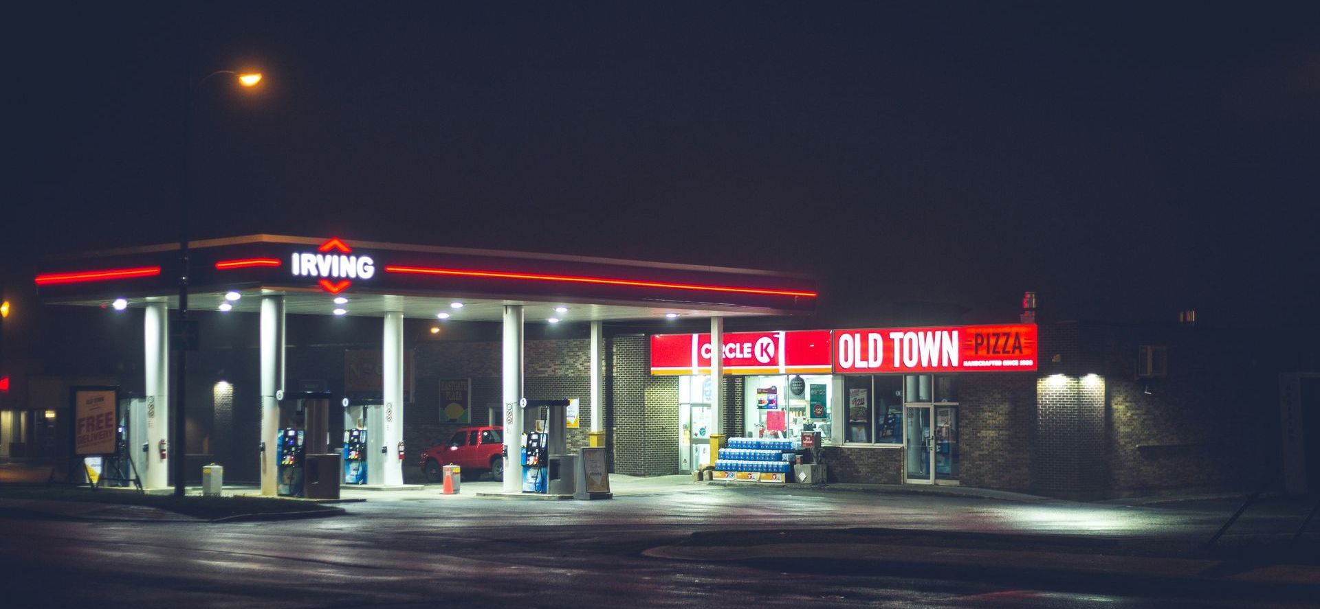 A red mustang is being pumped with gas at a gas station.