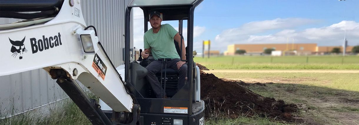 A man is sitting in the cab of a bobcat excavator.