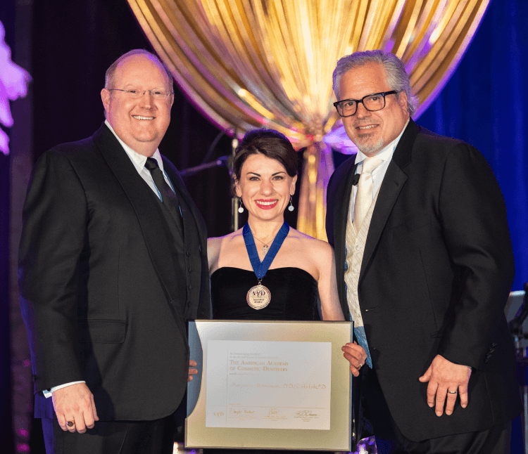 A woman in a black dress is standing between two men holding a certificate