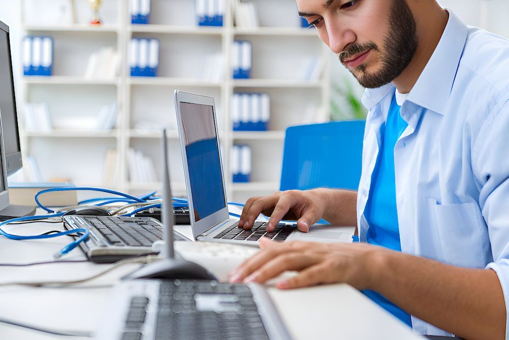 A Man Is Sitting At A Desk Using A Laptop Computer — Oz Data Tech in Forster, NSW