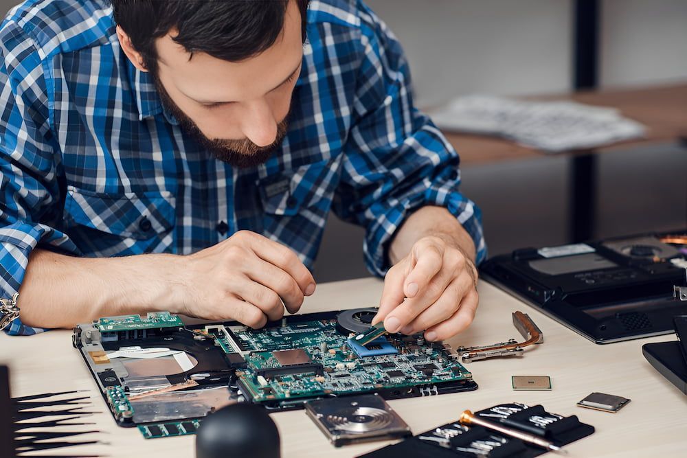 A Man In A Plaid Shirt Is Working On A Laptop Computer — Oz Data Tech in Forster, NSW