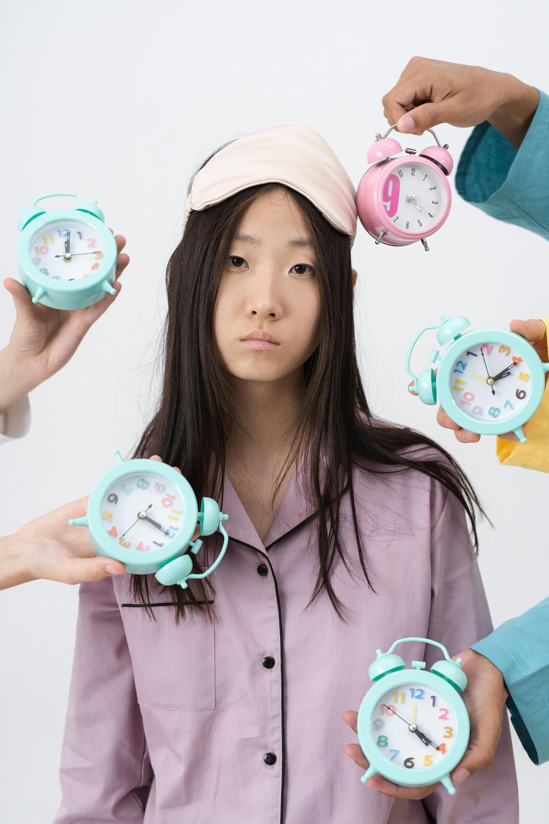 Young woman holding alarm clocks, looking tired and restless, symbolizing sleeplessness or insomnia