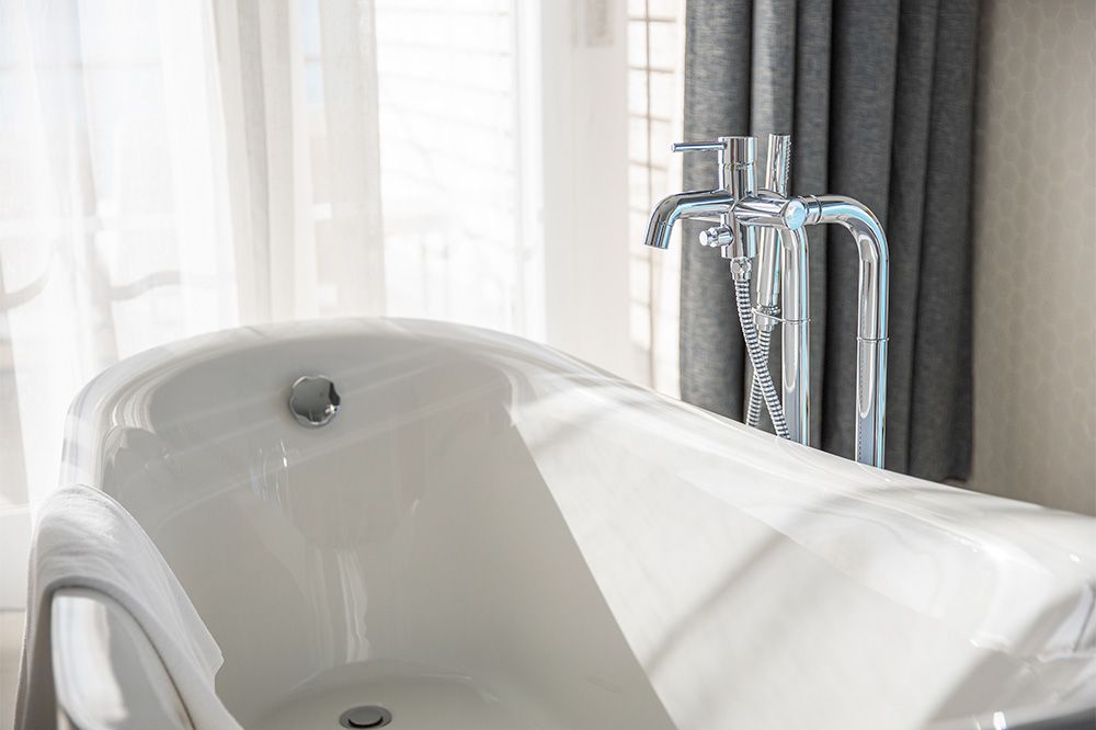 A white bathtub with a chrome faucet in a bathroom next to a window.