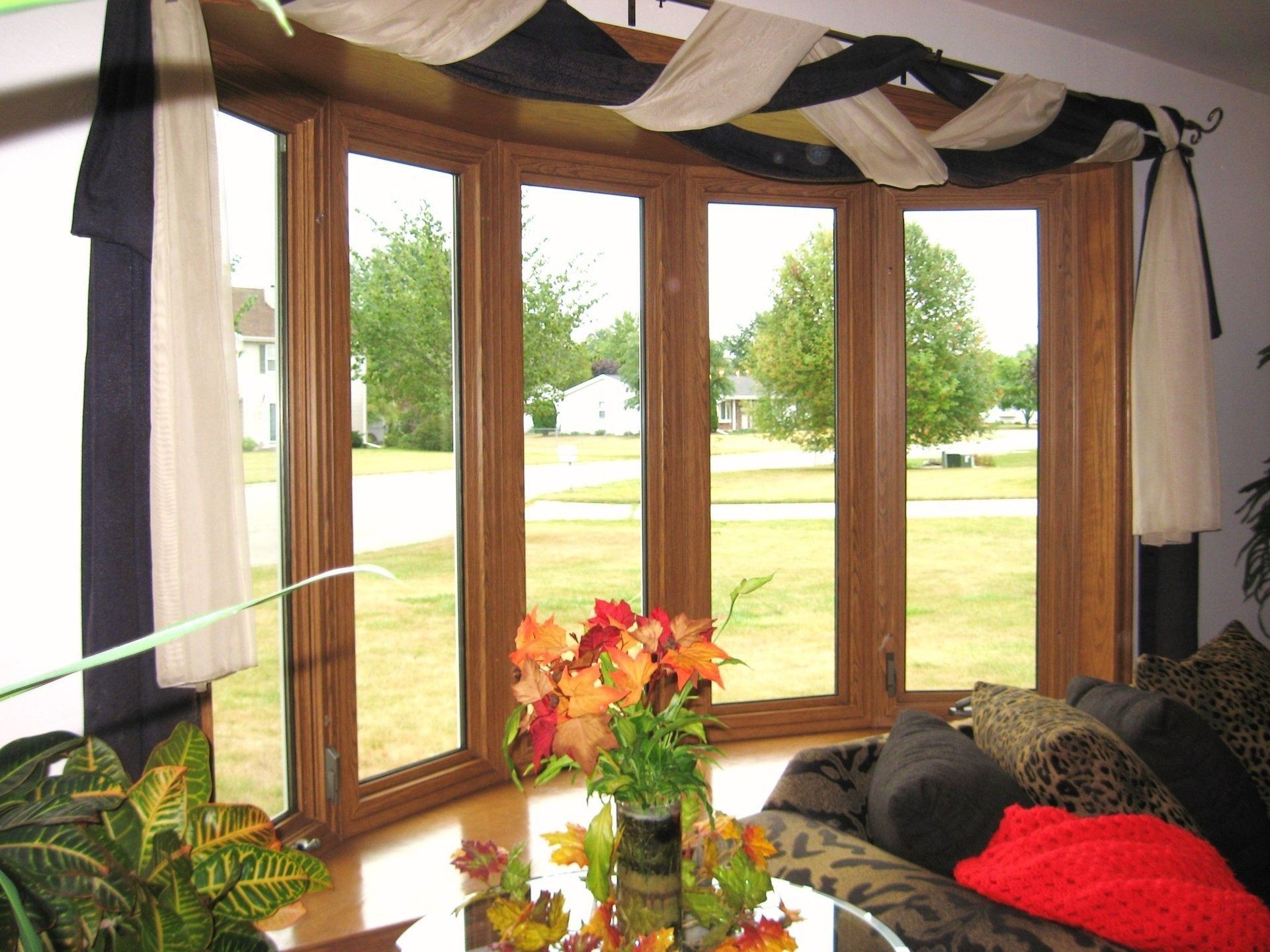 Living room bay window with striped valance, sofa, and vase of flowers overlooking a green yard