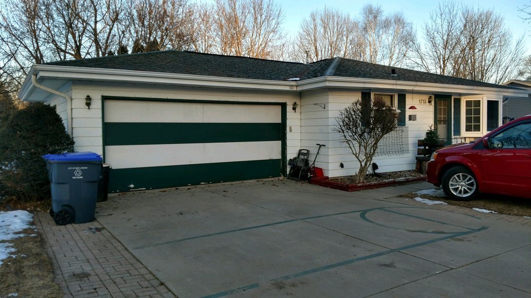 Suburban house with striped garage door, blue bin, and red car in the driveway at dusk
