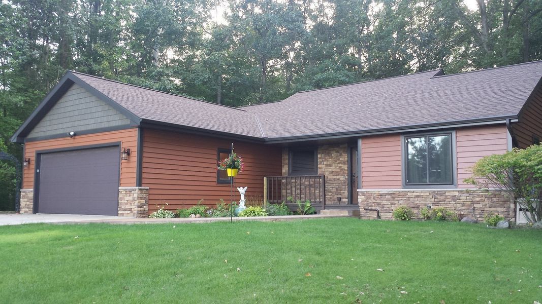 Single-story brick house with attached garage, dark roof, and a green lawn in front