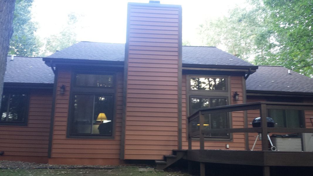 Wood-paneled house exterior with central chimney and deck in a wooded setting
