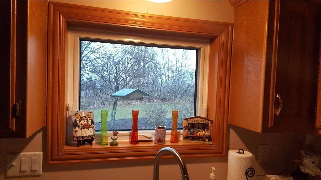 Kitchen sink window with rain outside, framed by wooden cabinets and small items on the sill