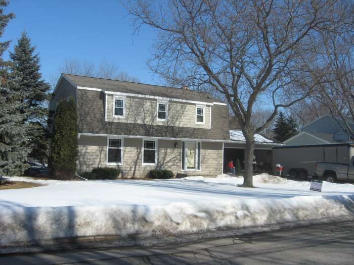 Snowy suburban house with bare trees and a garage in winter.