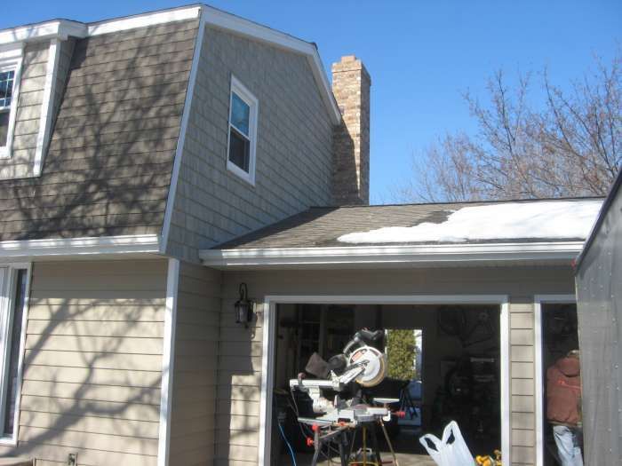 House with garage open; a person on a tricycle sits inside under a snowy roof.