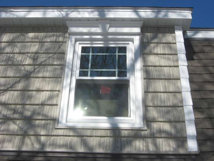 White-framed window on a gray-shingled house exterior under bright sunlight.