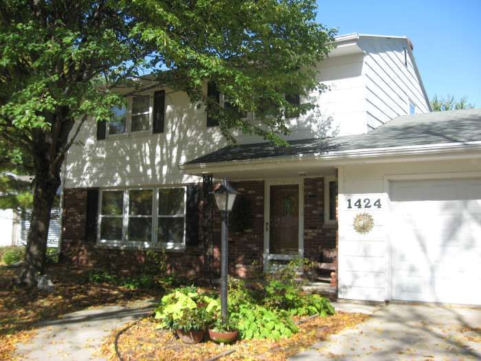 Two-story house with white siding, front porch, garage, and leafy front yard in daylight