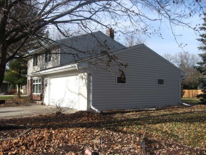 White house with a garage, gray roof, and autumn trees in the yard
