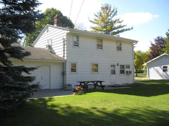 White two-story house with attached garage, picnic table, and green lawn on a sunny day