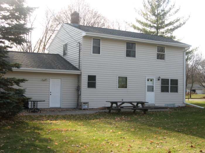 White two-story house with a picnic table and lawn in front, viewed from the backyard
