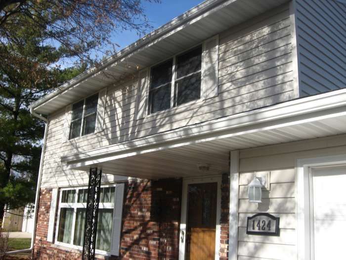 Two-story townhouse exterior with brick and siding, front porch, and house number plaque