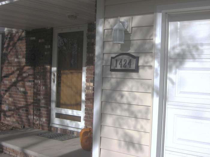 Front porch with brick wall, white door, and house number 1424 beside a garage.