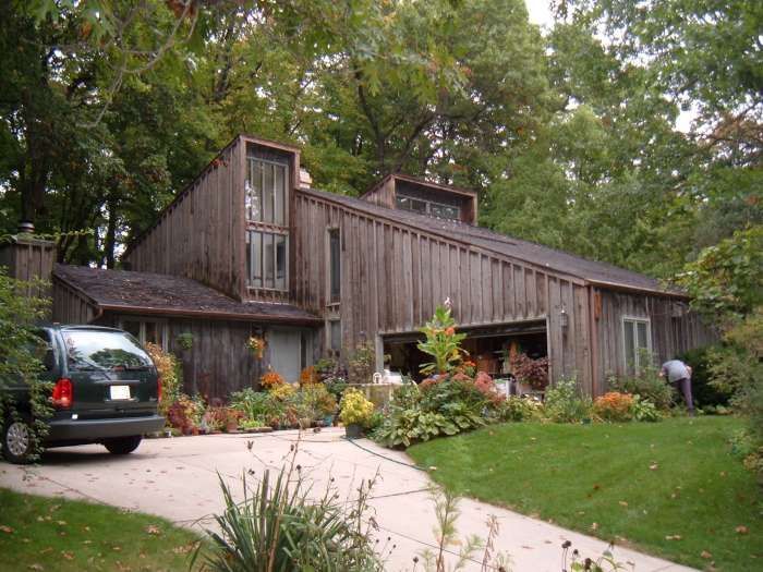 Wooden house with slanted roof, front garden, and a parked car on the driveway.
