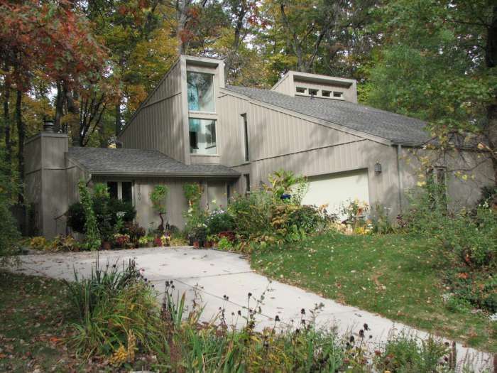 Modern house with sloped roof and large windows surrounded by trees, shrubs, and a curved driveway