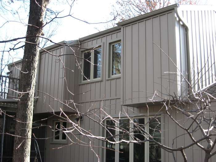 Two-story gray house with trees and bare branches in the foreground