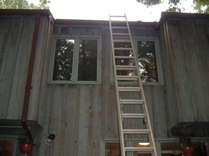 Wooden ladder leaning against a weathered house between two windows