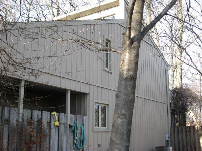 Gray house exterior with leafless trees and a small covered porch