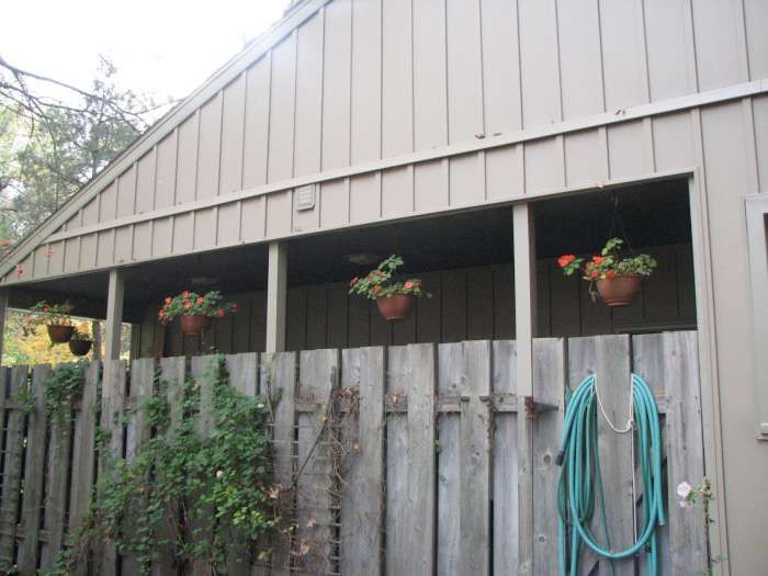 Barn with hanging flower baskets behind a weathered wooden fence and garden hose