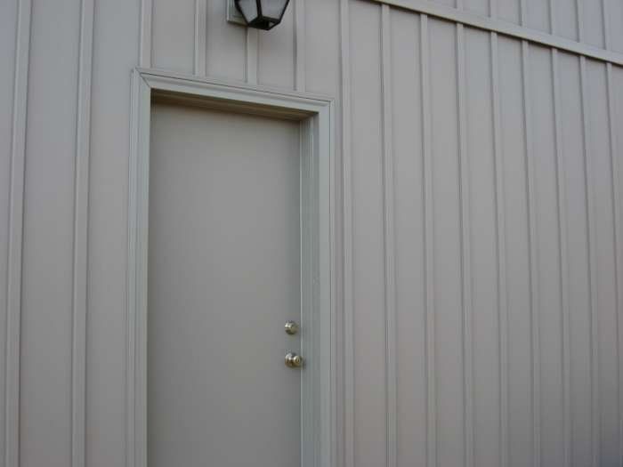 Gray metal building wall with a closed door and an exterior light above it