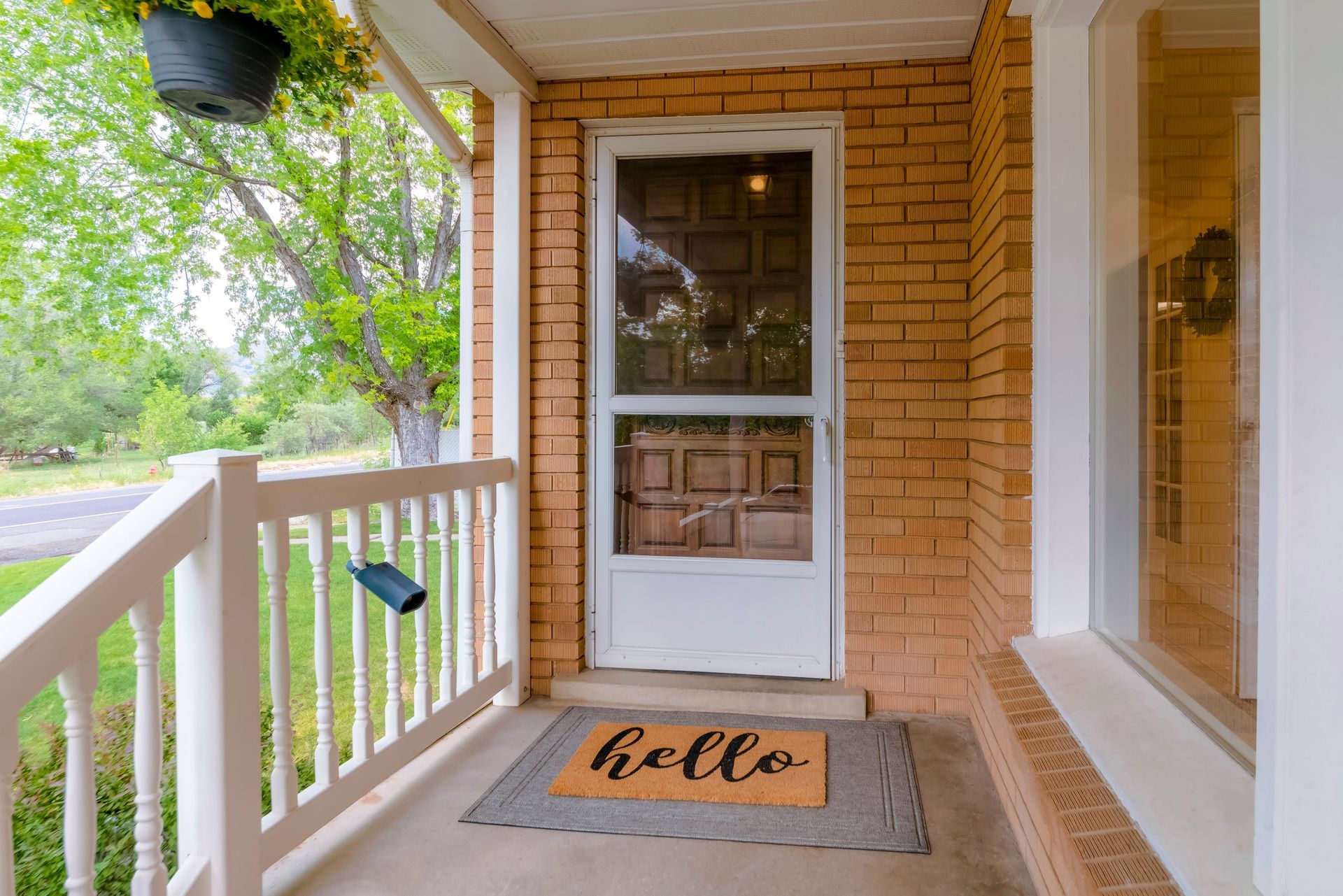 Front porch with white railing, brick wall, glass door, and a “hello” doormat.