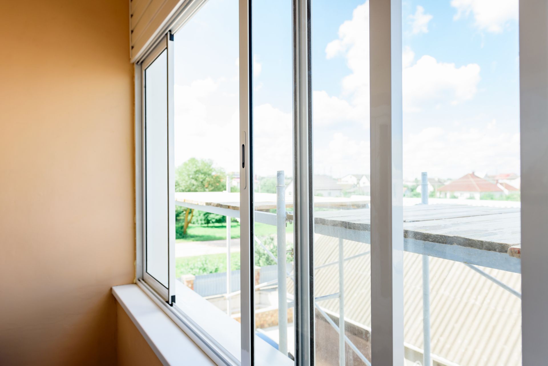 Sunlit window with open blinds overlooking rooftops and blue sky