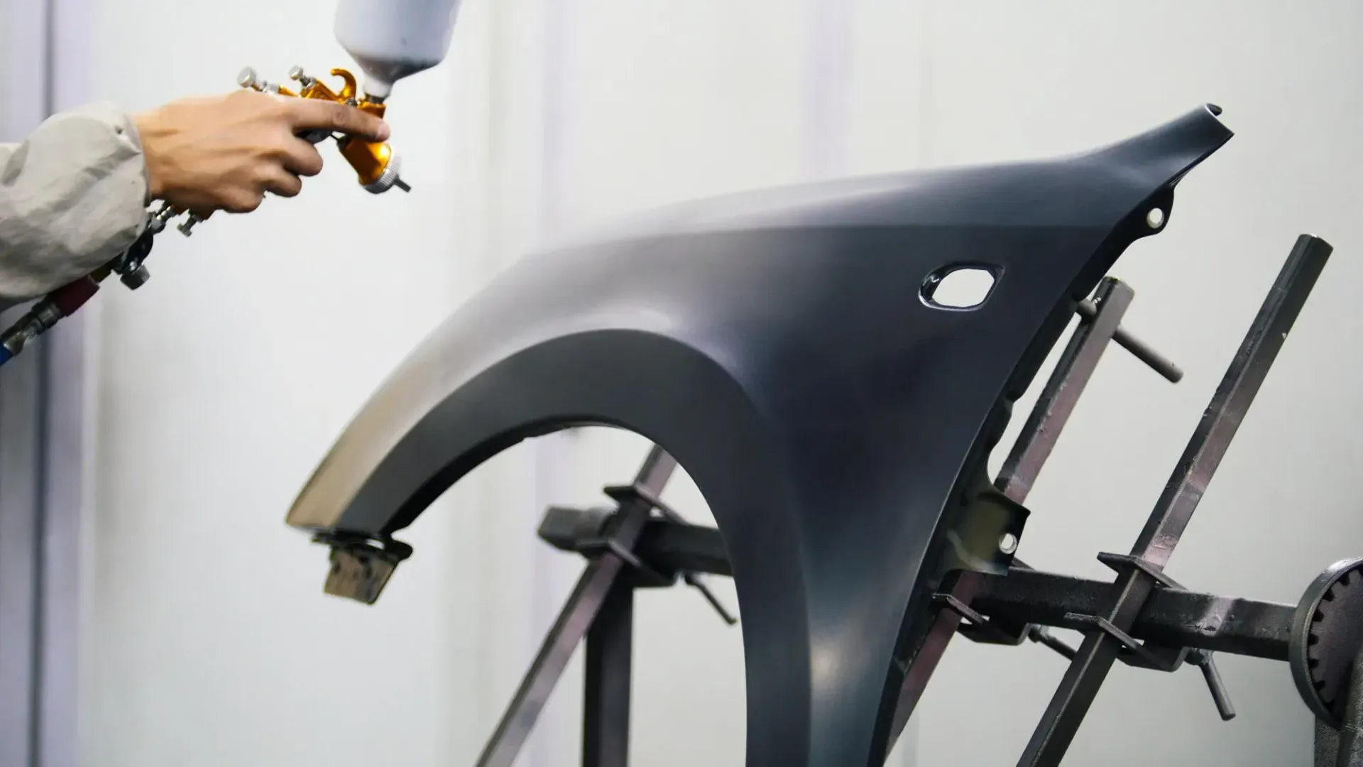 A person is spraying paint on a car fender.