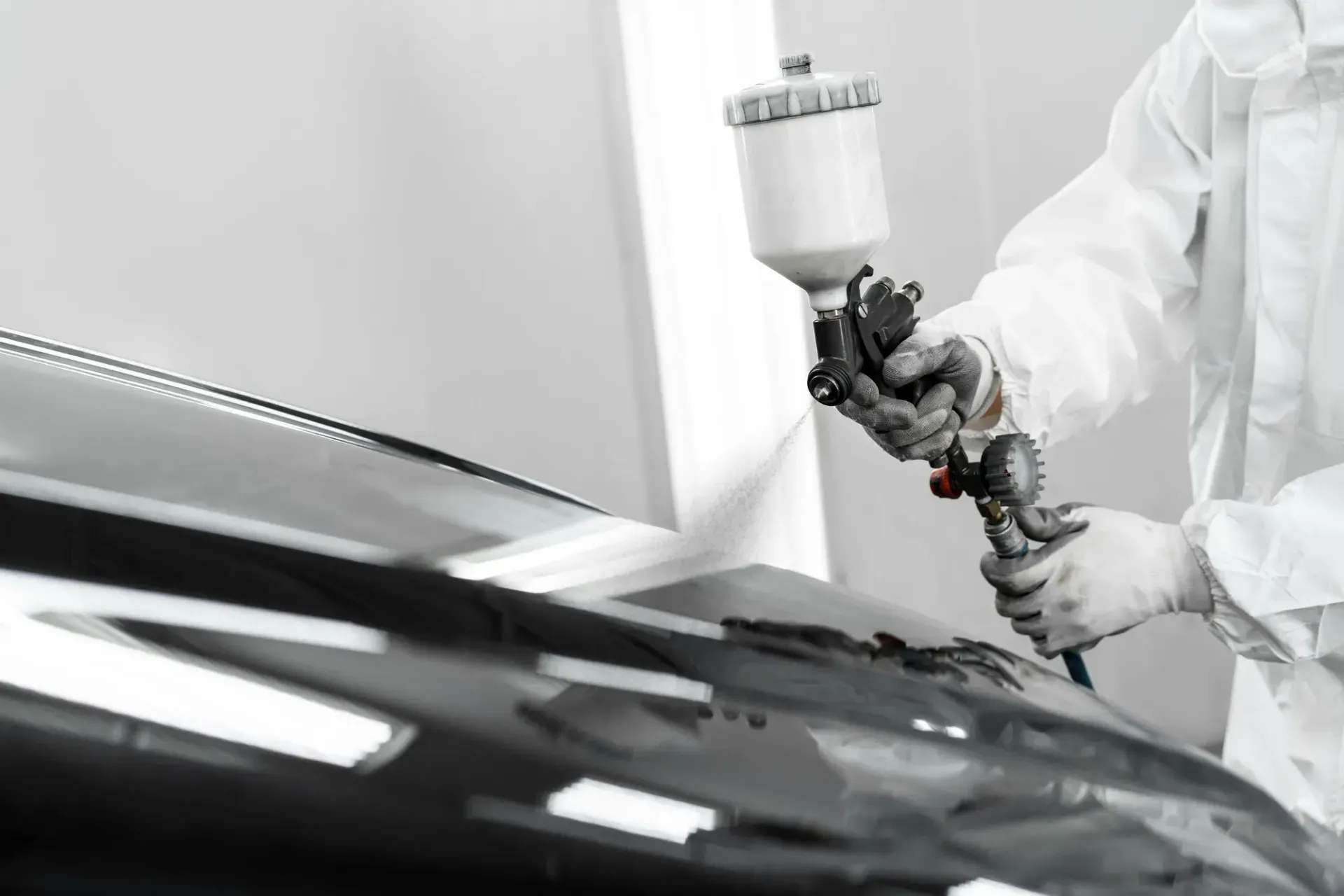 A man is spraying paint on the hood of a car.