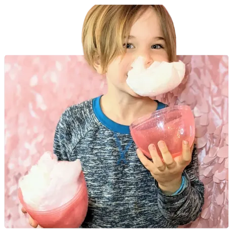 A young boy is blowing cotton candy out of a cup