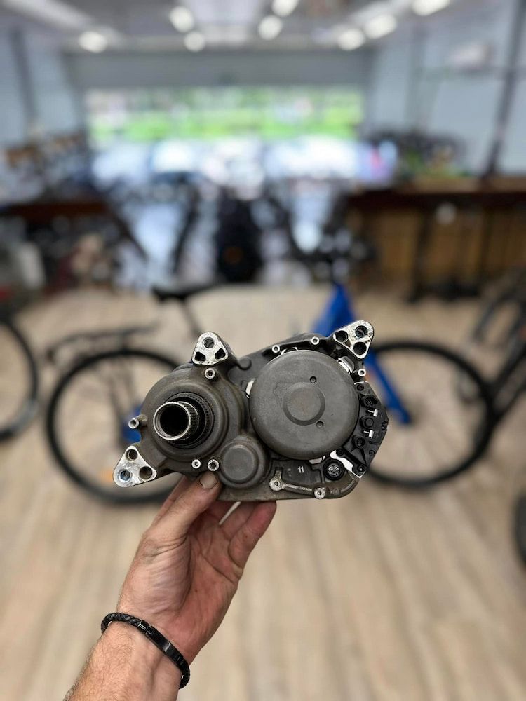 Hand holding a bicycle motor. A blurred bicycle and shop interior are in the background — Grafton City Cycles in Grafton, NSW